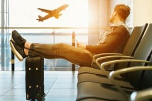 un homme attend à l'aéroport les deux pieds posés sur sa valise