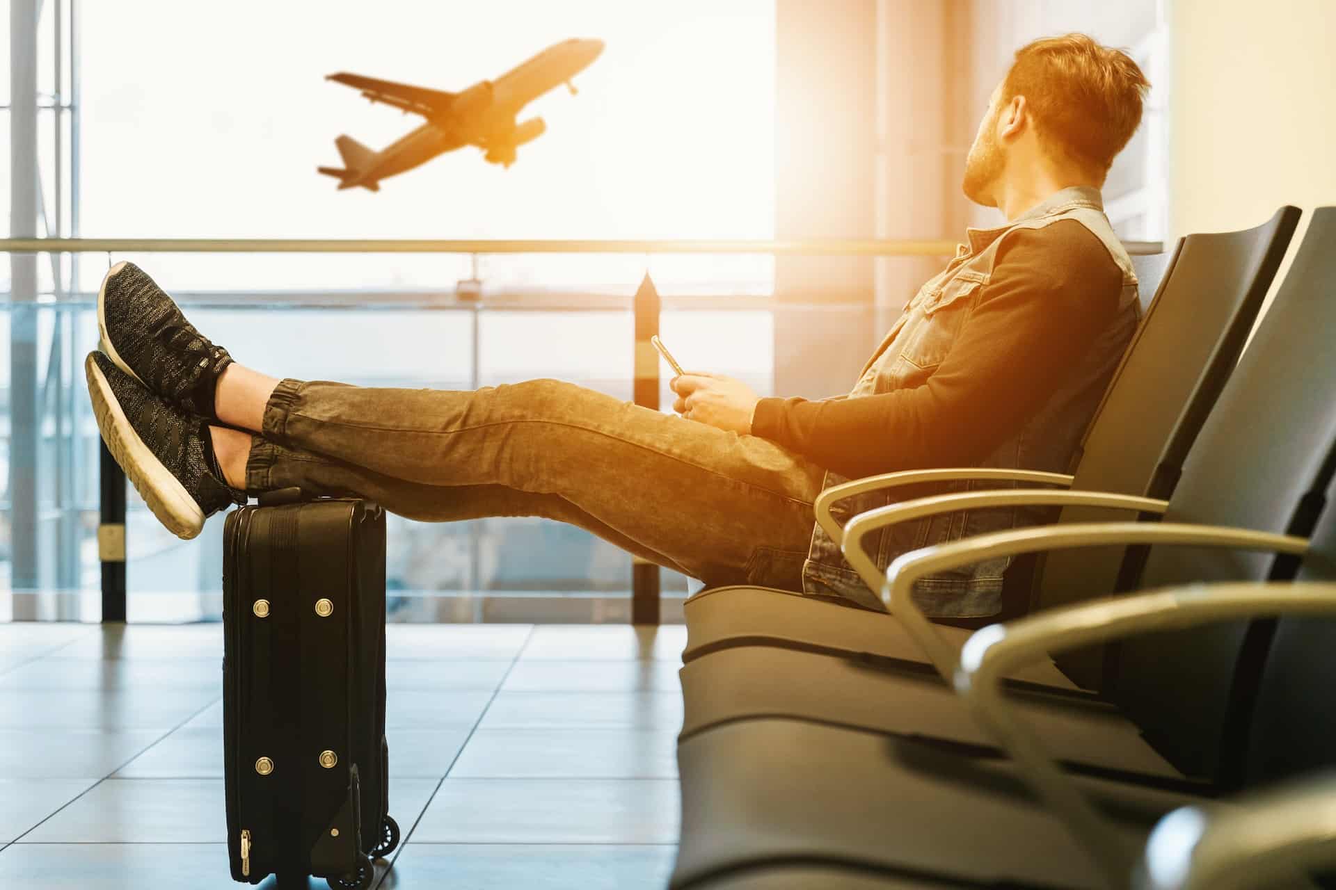 Un homme assis attend son avion les pieds posés sur sa valise