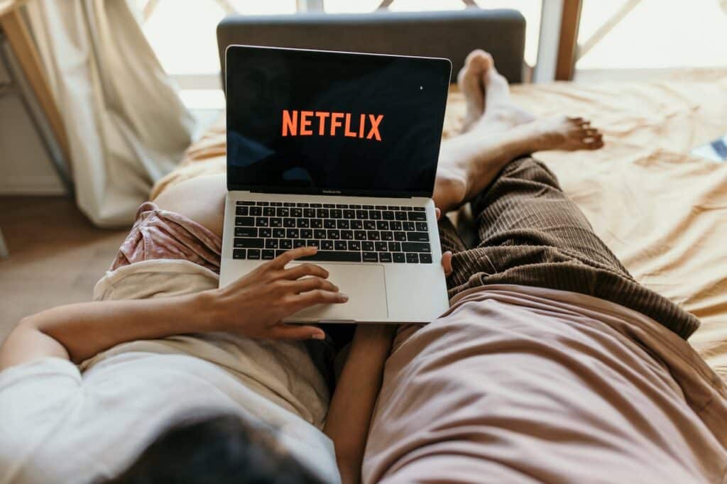 Un couple regarde Netflix sur un ordinateur portable, allongé dans leur lit