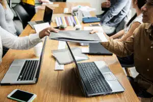 une réunion de travail en entreprise, des ordinateurs sont ouverts sur une grande table en bois clair