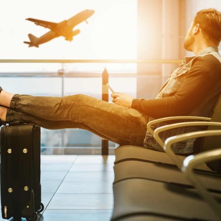 Un homme assis attend son avion les pieds posés sur sa valise